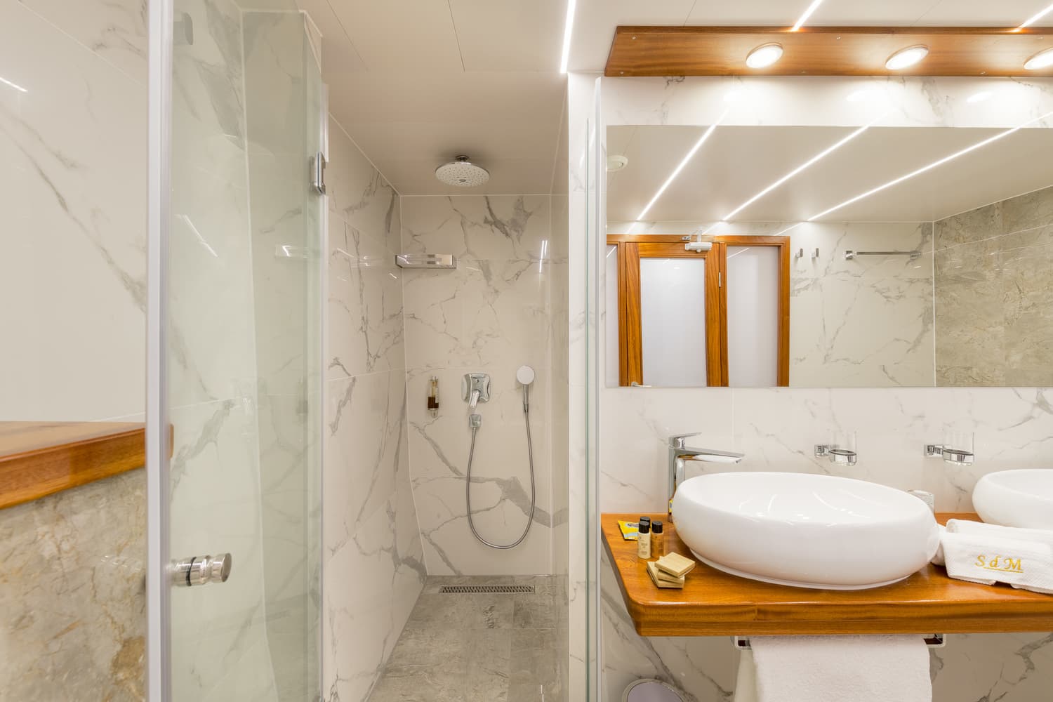 Modern bathroom with marble shower and vessel sink on wooden vanity, likely on a boat.