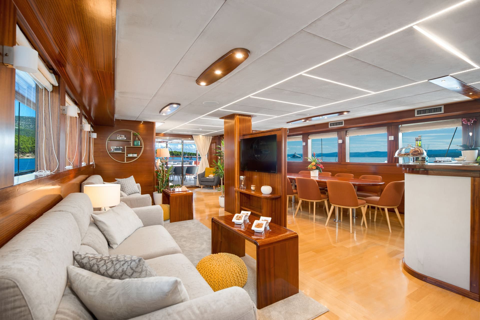 Lounge and bar interior of a yacht with wood paneling and sea view.