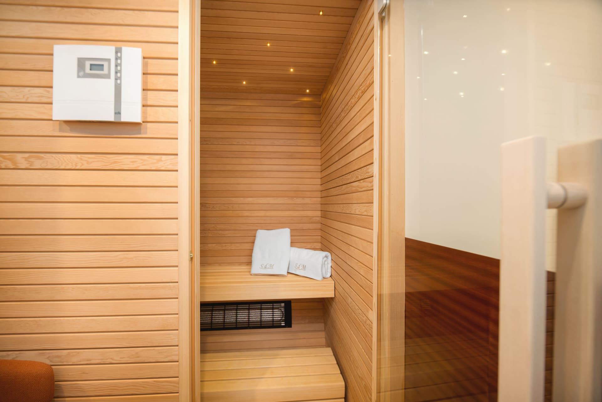 Interior of a modern wooden sauna cabin with rolled towels and a control panel.