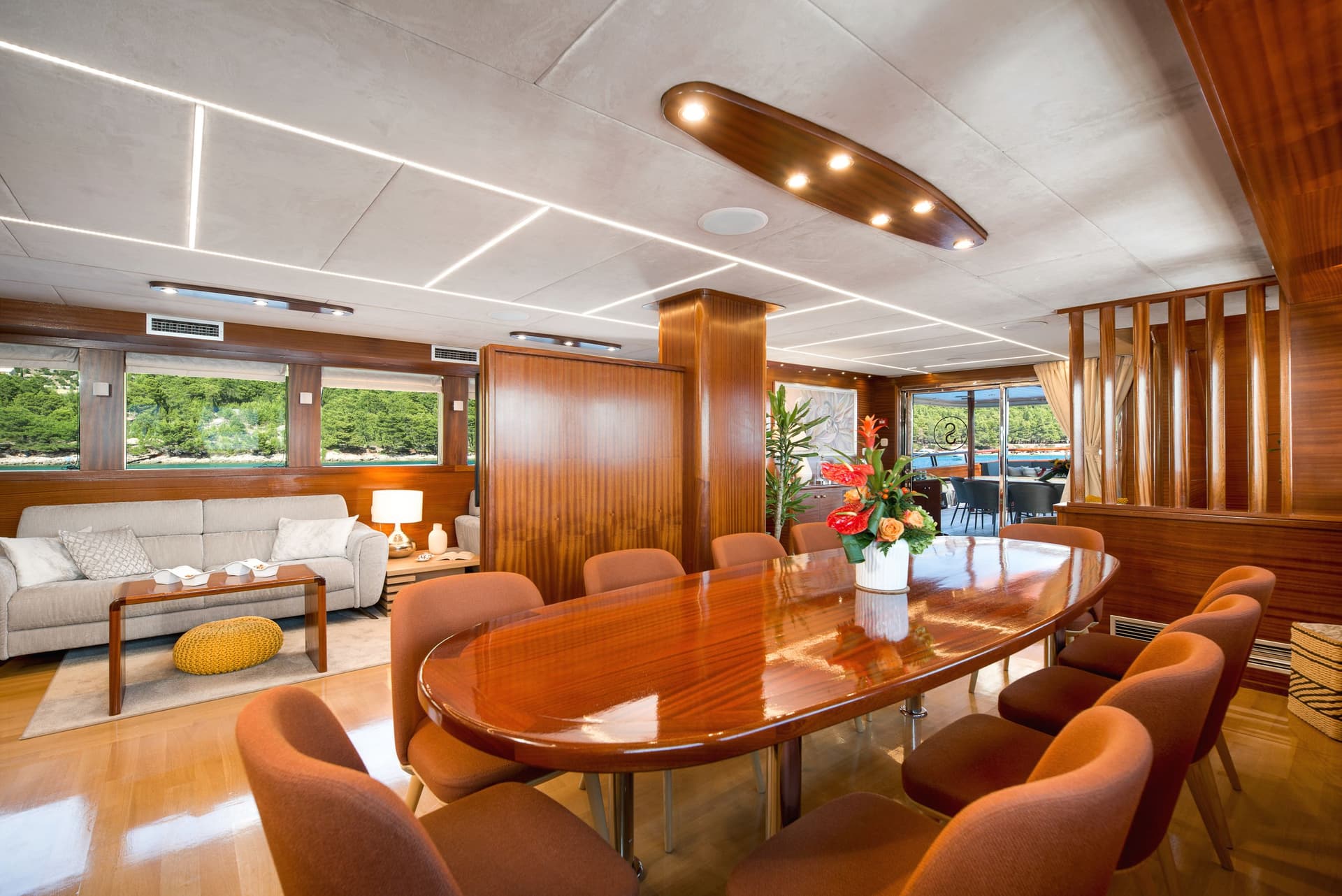 Yacht interior dining area with wood paneling, plush seating, and view of green coastline.