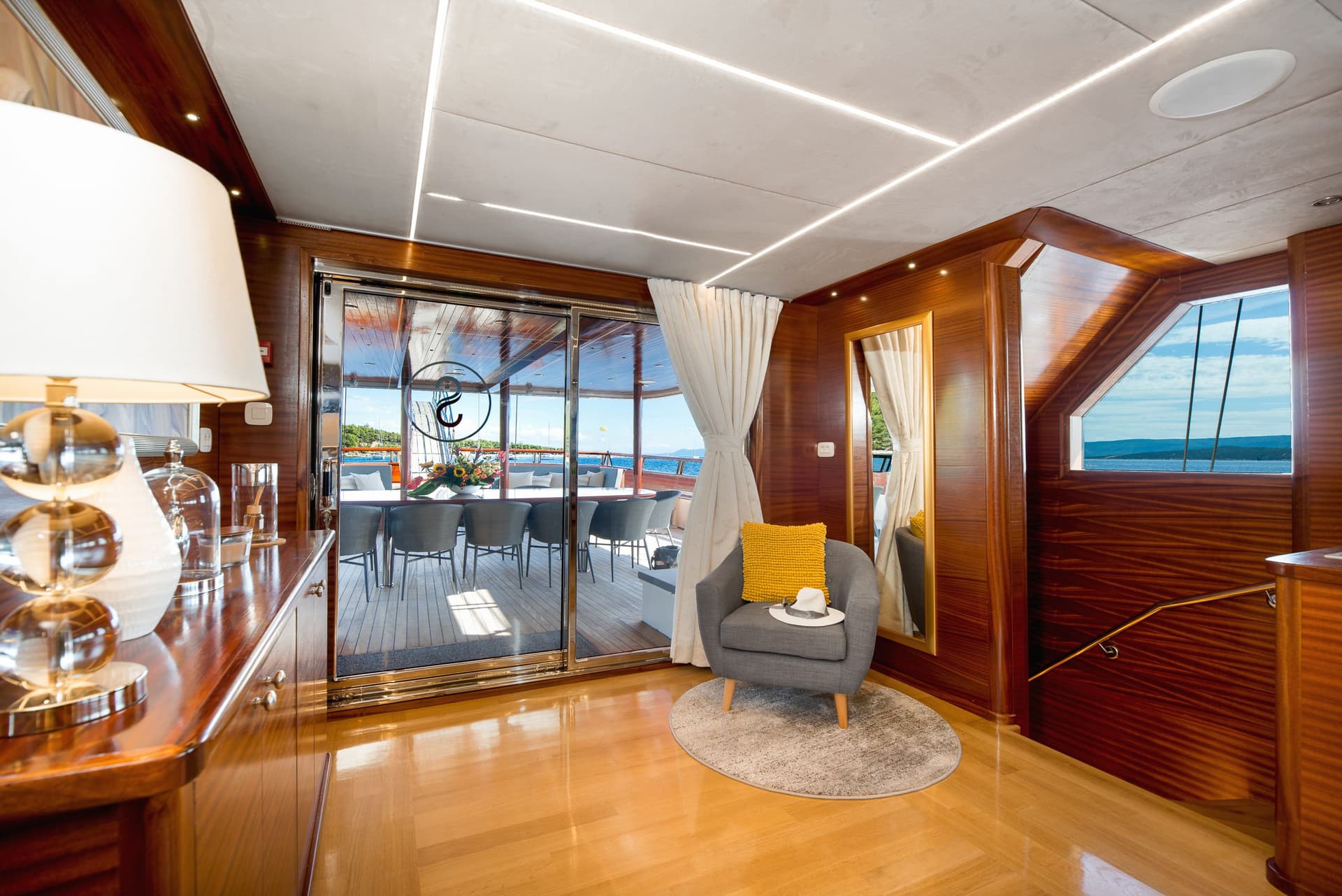 Interior yacht lounge with wood paneling, view of outdoor dining area, and blue sea.