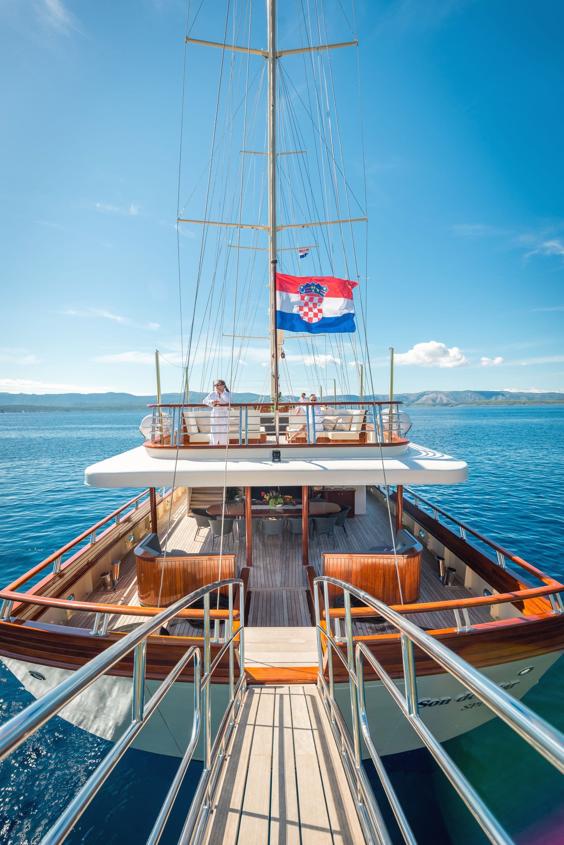 View from gangway onto wooden yacht deck with Croatian flag, mountains in background.