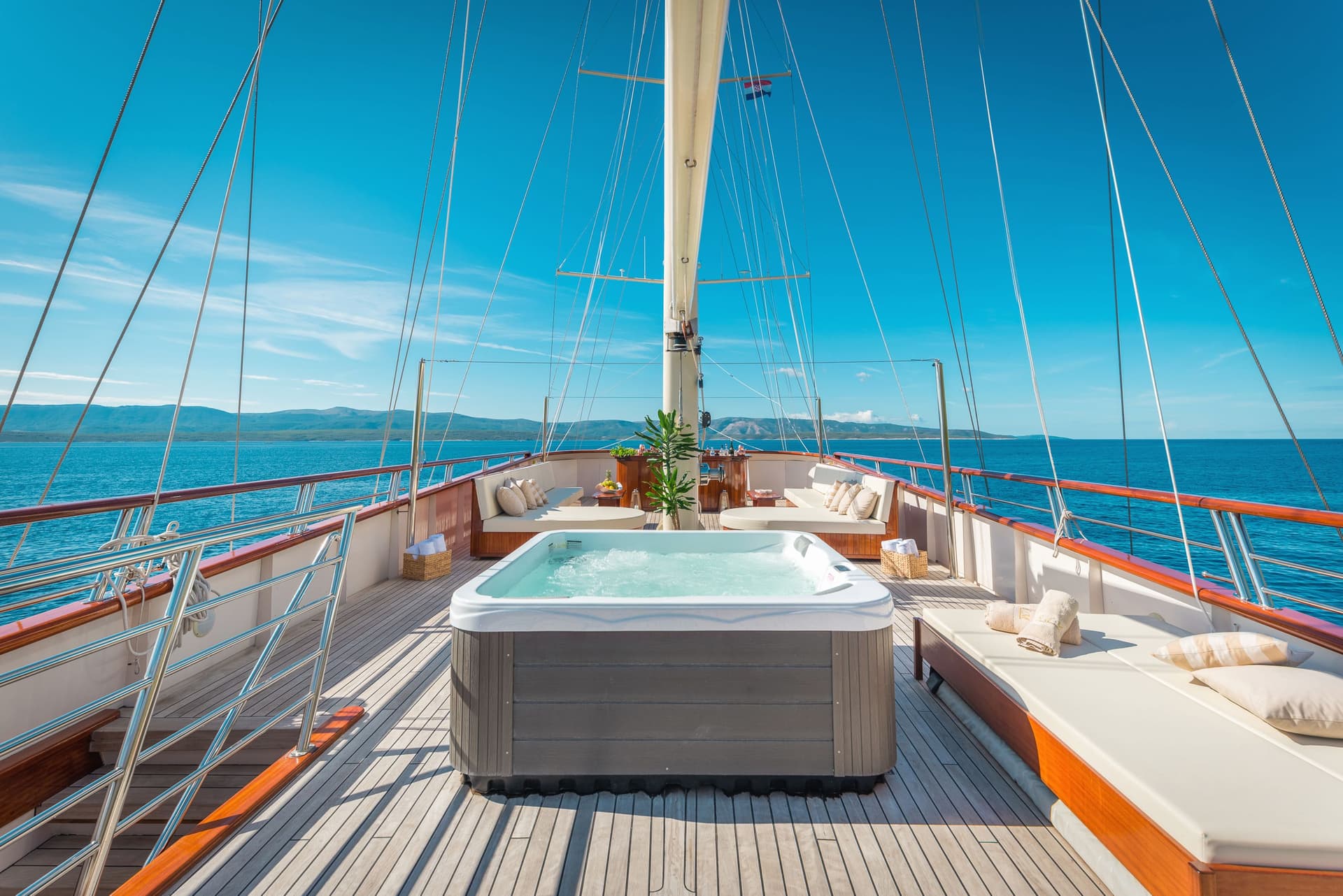 Jacuzzi on a yacht deck with teak flooring, overlooking blue sea and distant mountains.