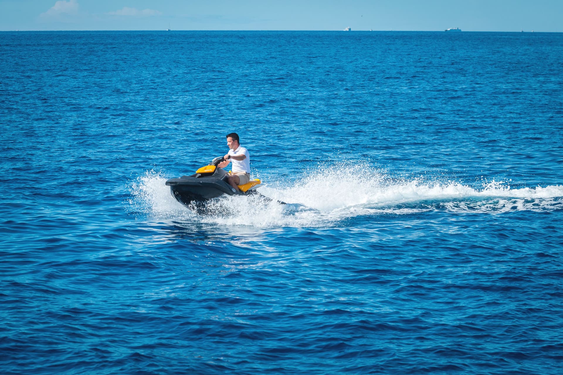 Man riding a black and yellow jet ski, creating white spray on deep blue ocean water