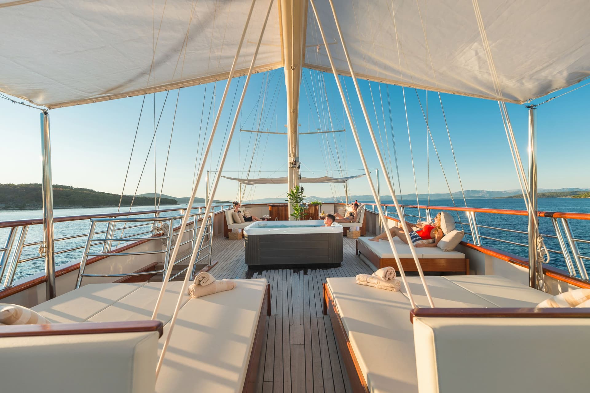 Lounge area on a boat deck with sunbeds, a hot tub, and island scenery.