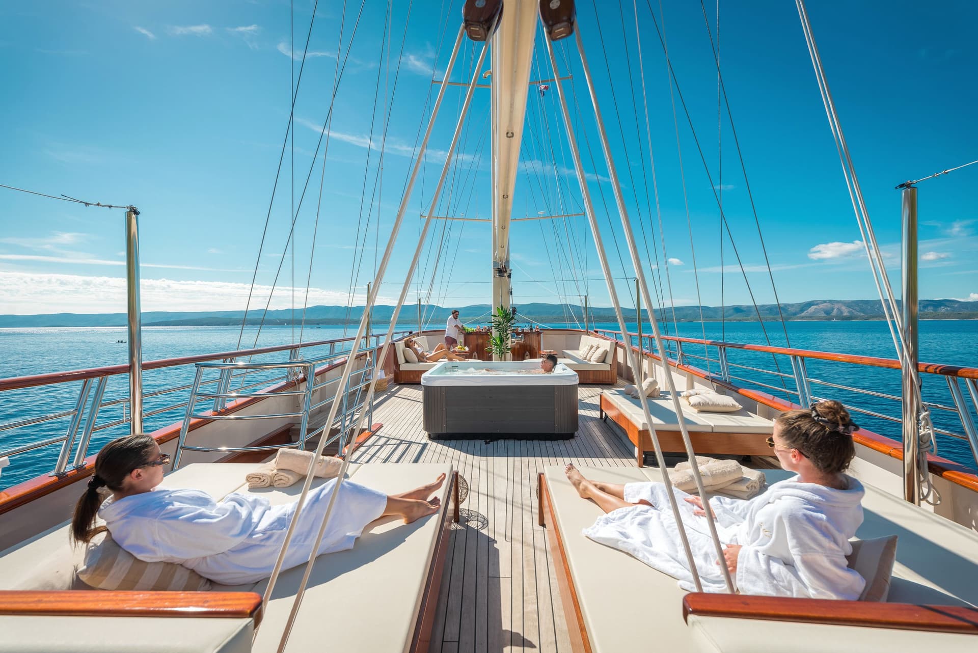 Sunbathing on yacht deck with hot tub, overlooking blue sea and distant mountains
