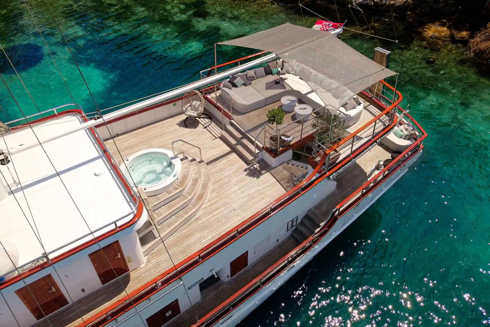 Yacht deck with hot tub and lounge area anchored in clear turquoise coastal water.