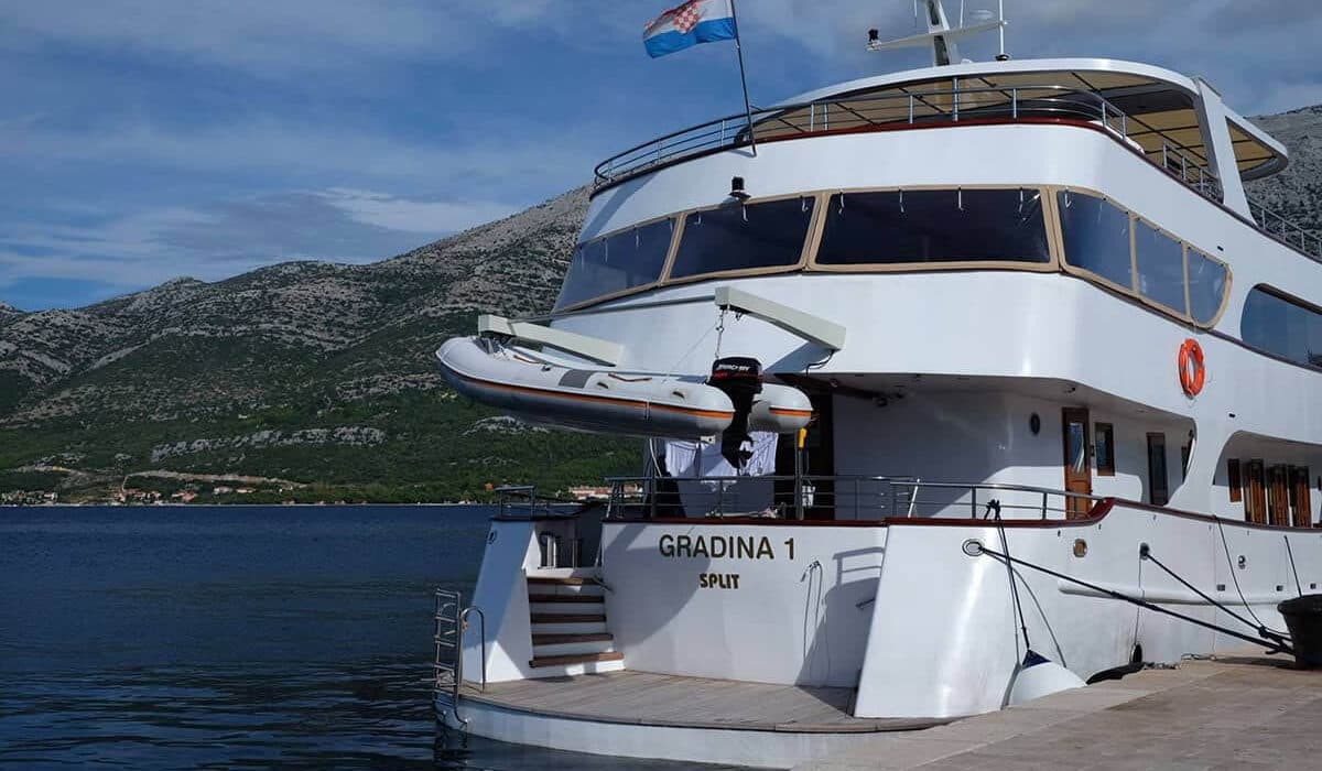 Yacht "Gradina 1 Split" docked, dinghy hanging off stern, with Croatian flag and mountains.