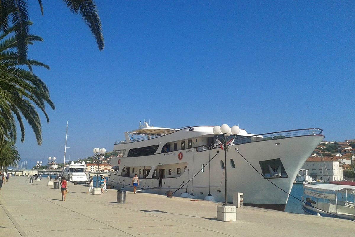 Large white yacht docked at promenade with palm trees and town in background