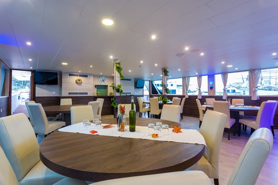 Dining room interior on a boat with views of docked ships through windows