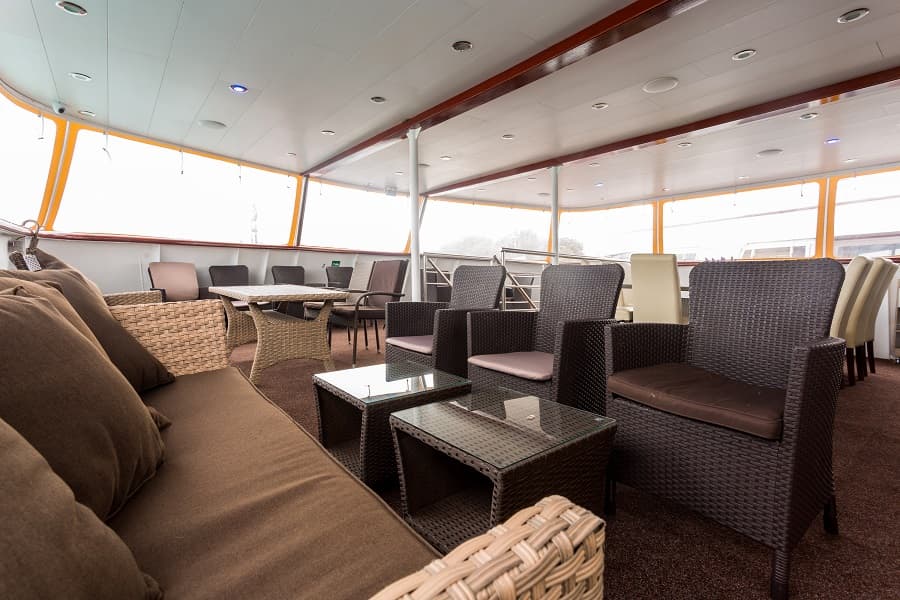 Lounge seating area with wicker furniture on an enclosed boat deck with bright windows