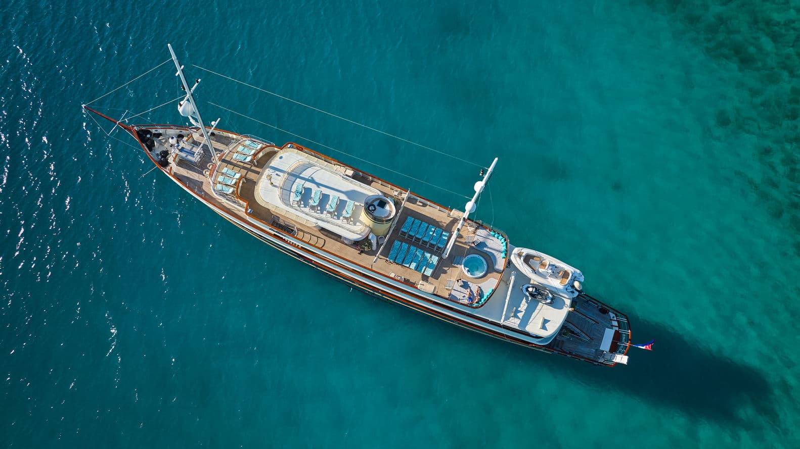 Aerial view of a luxury yacht anchored in clear turquoise coastal waters.