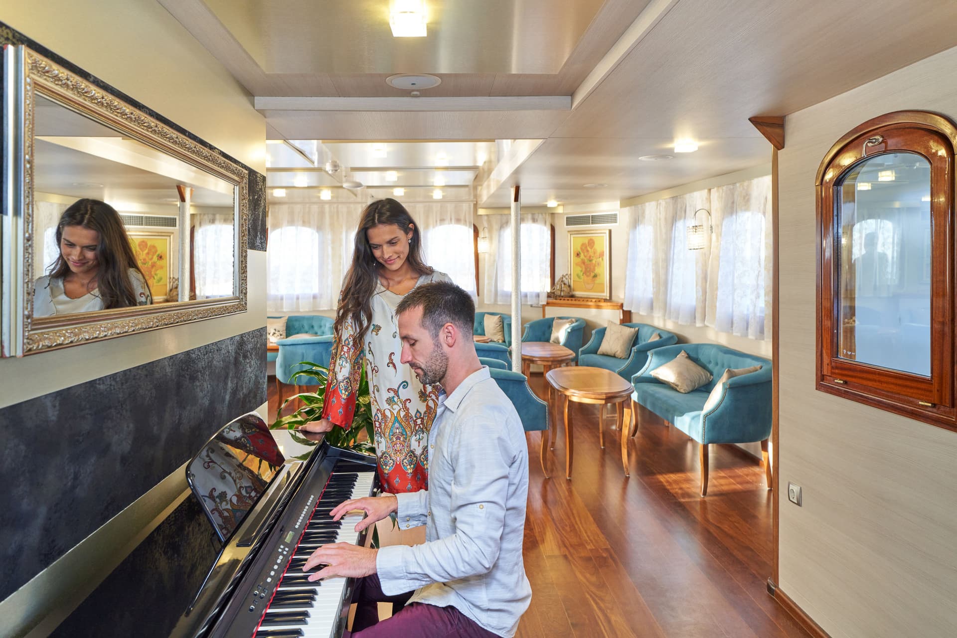 Man playing digital piano while woman watches in luxurious yacht lounge with blue seating.