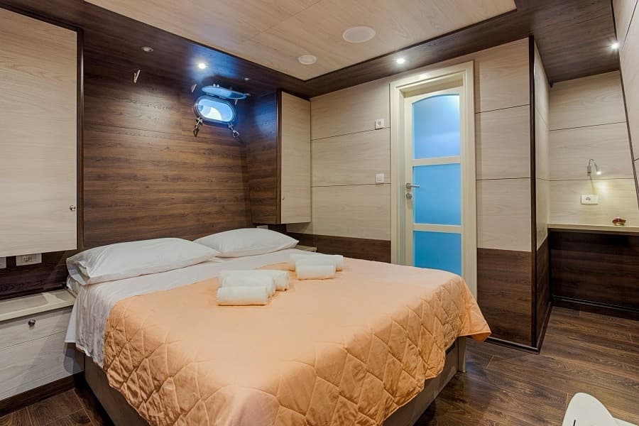 Double cabin bedroom with wood paneling, porthole, and peach bedspread