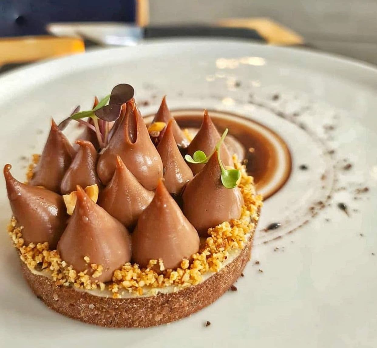 Chocolate tart with piped frosting, chopped nuts, and microgreens on a white plate.