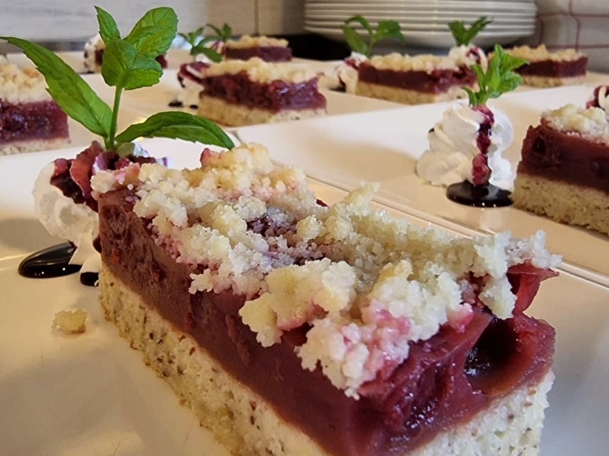 Plum crumble cake slice with whipped cream and mint garnish on white plates