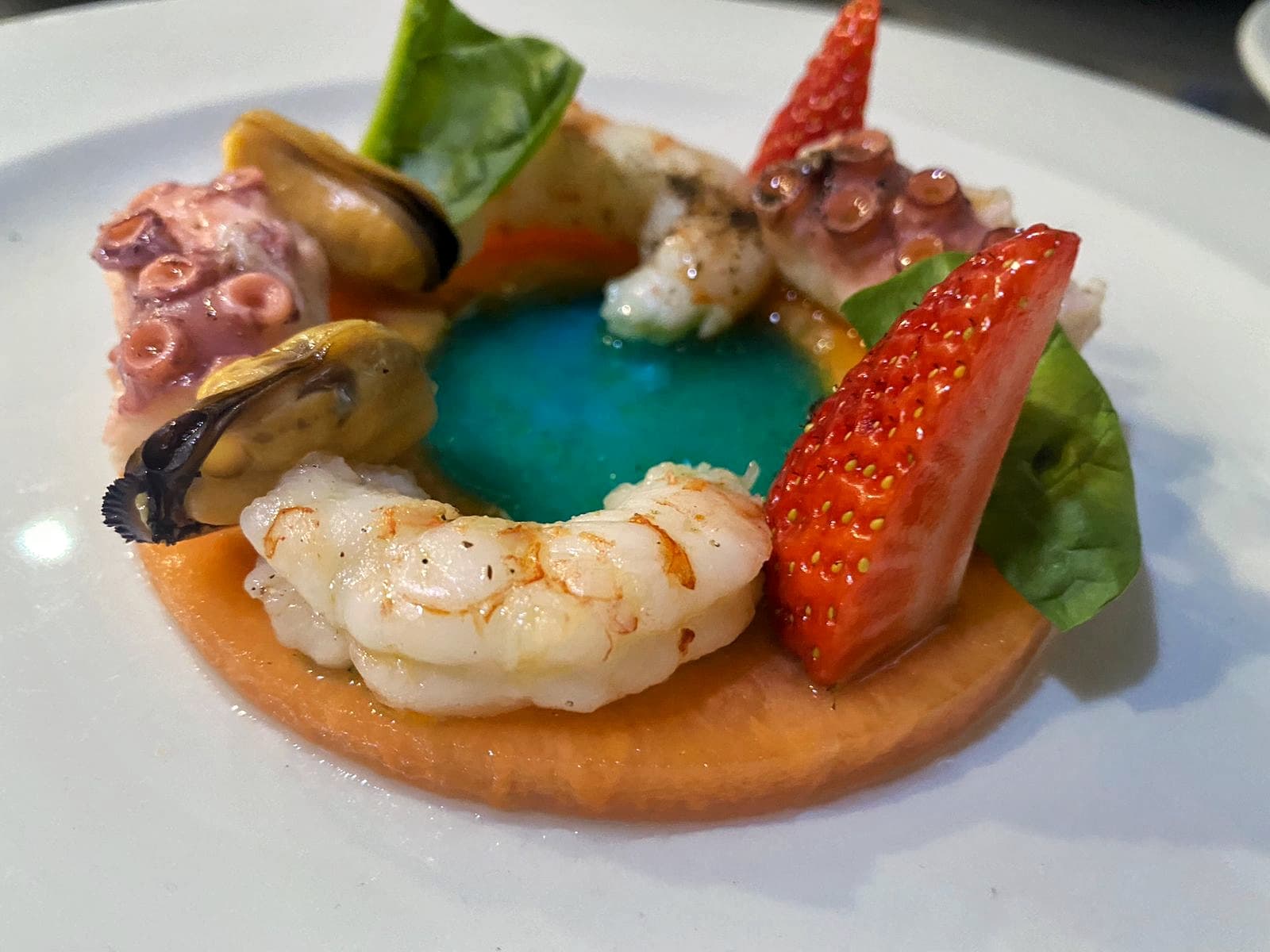 Seafood appetizer with shrimp, octopus, mussels, strawberry, and blue gel on orange base