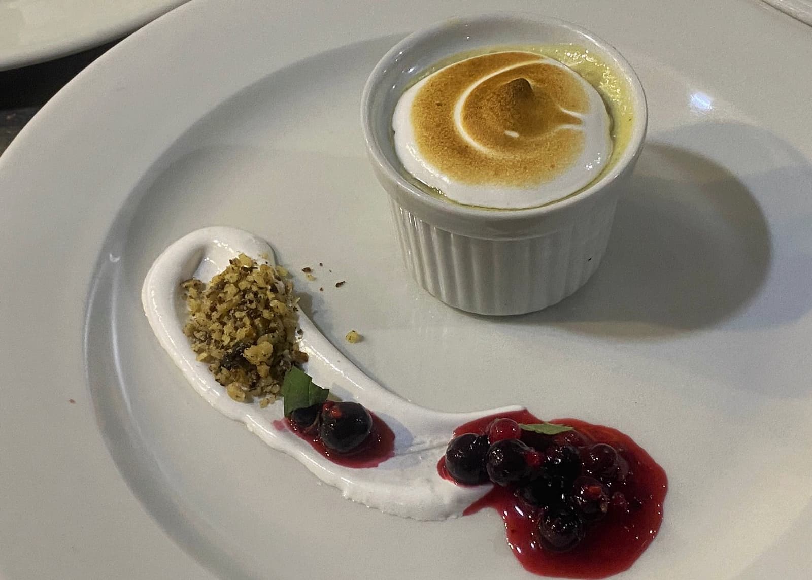 Dessert with torched meringue in a ramekin, nuts, and berry compote on a white plate.