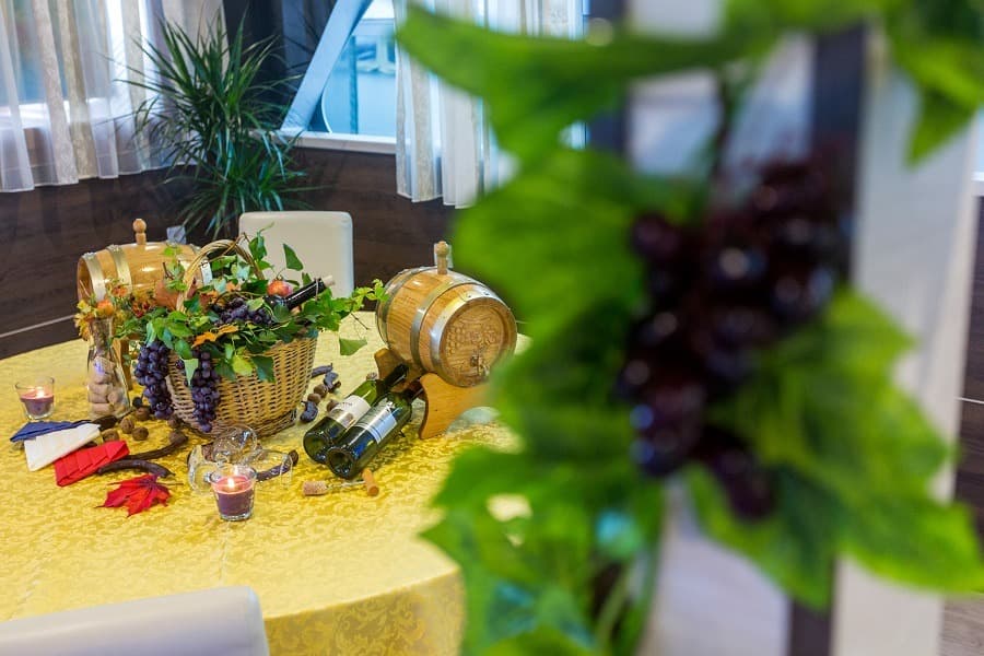 Wine harvest decoration with grapes, barrels, bottles, and candles on a yellow tablecloth.