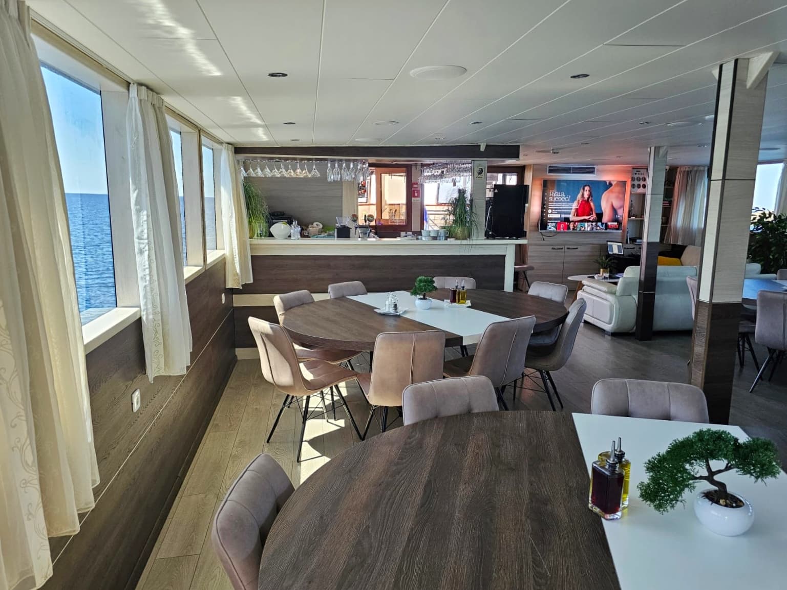 Dining area with tables and chairs inside a boat looking out at the sea.