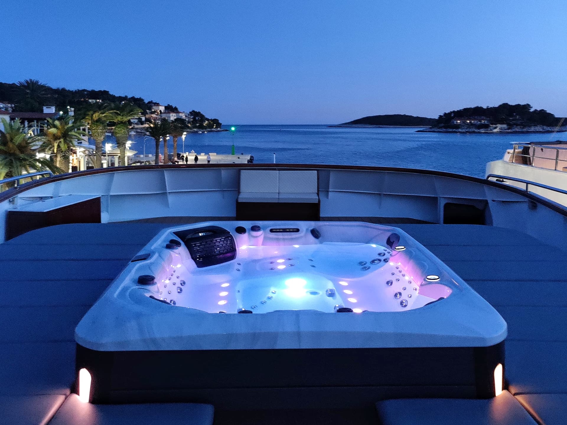 Illuminated outdoor jacuzzi on a boat deck overlooking a coastal town at dusk