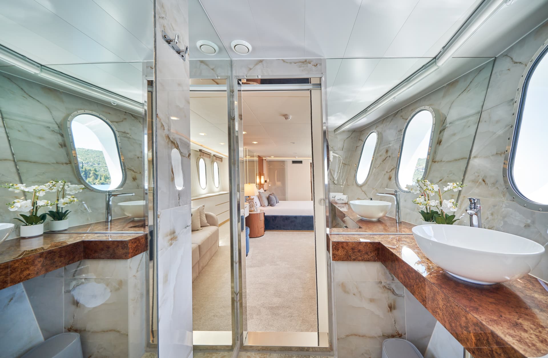 Luxury yacht bathroom with marble vanity, vessel sink, and view of green coastline through porthole.