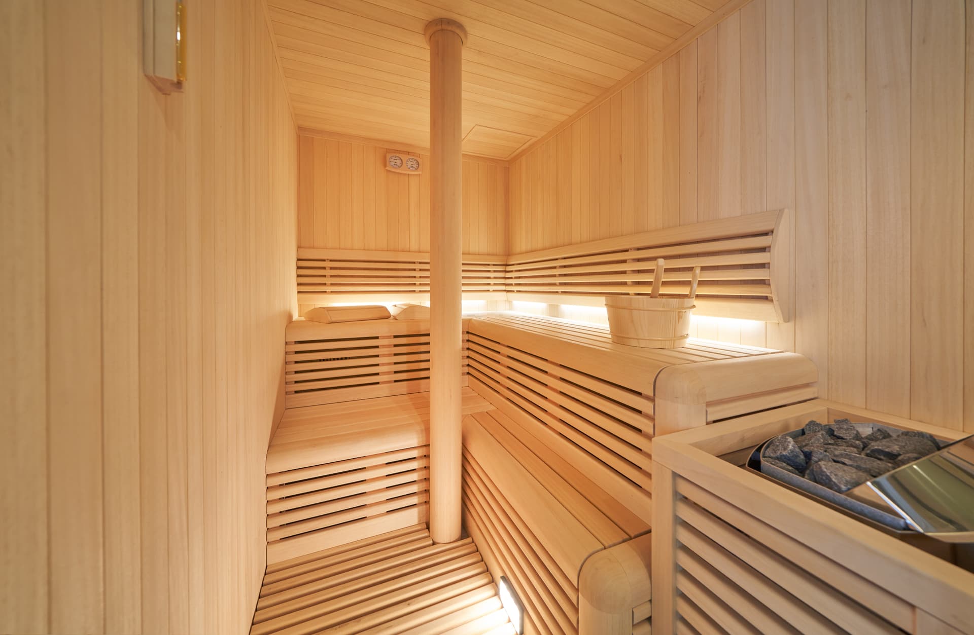 Interior of a modern wooden sauna with tiered benches, bucket, and hot stones.