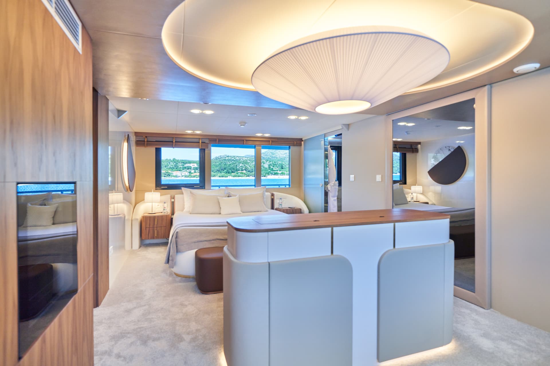 Modern yacht cabin bedroom with view of green coastline and blue sea water.