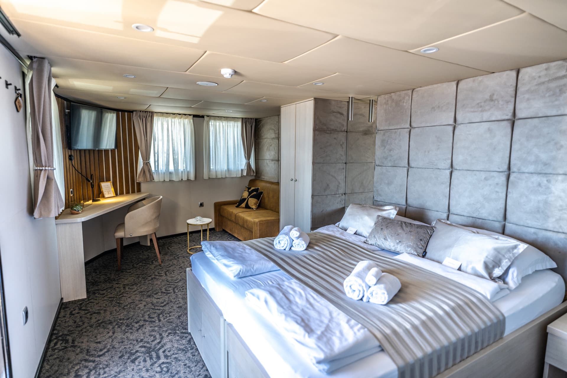 Modern cabin bedroom with bed, desk, and small sofa, likely on a boat or ship.