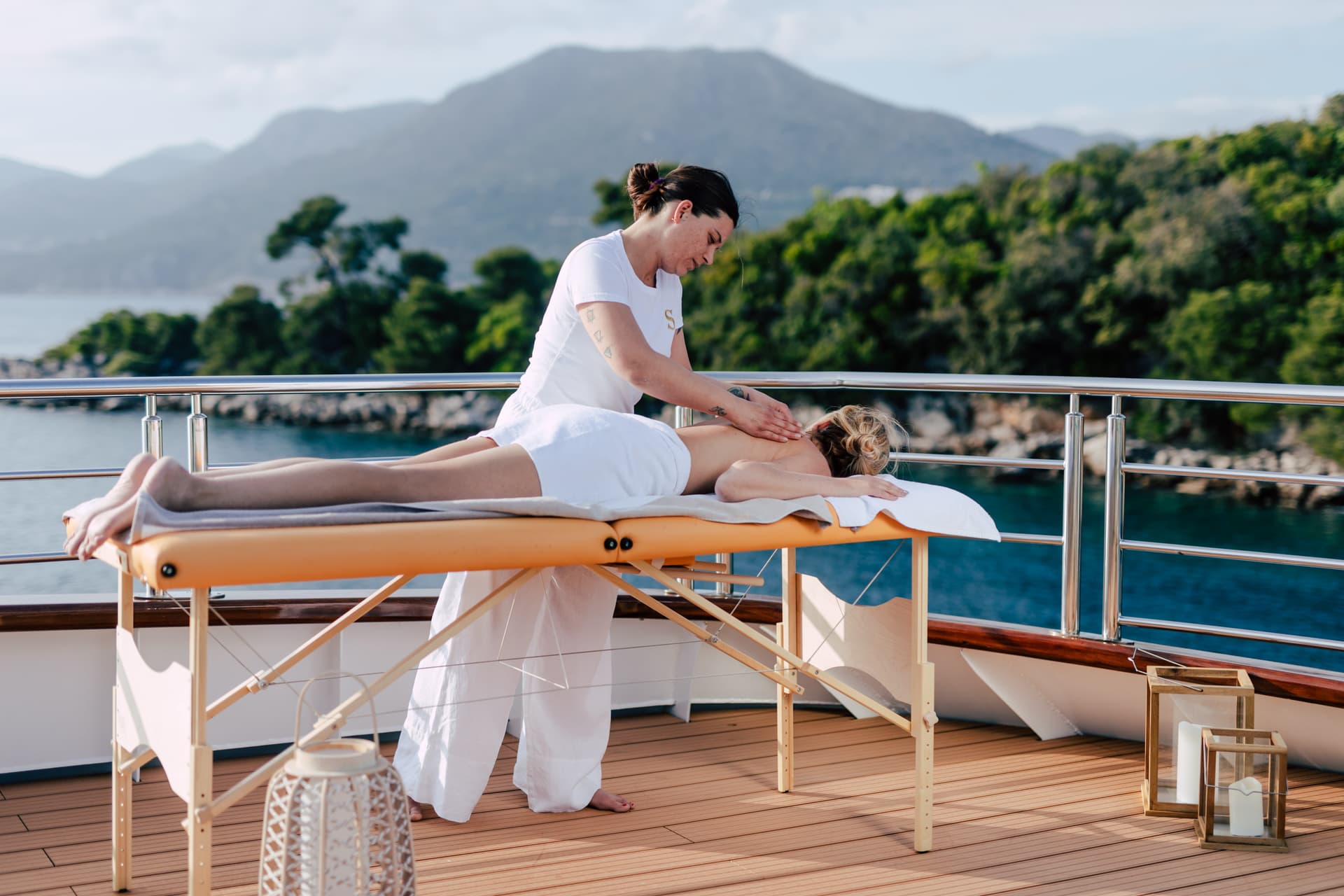 Woman receiving back massage on yacht deck with mountains and sea in background