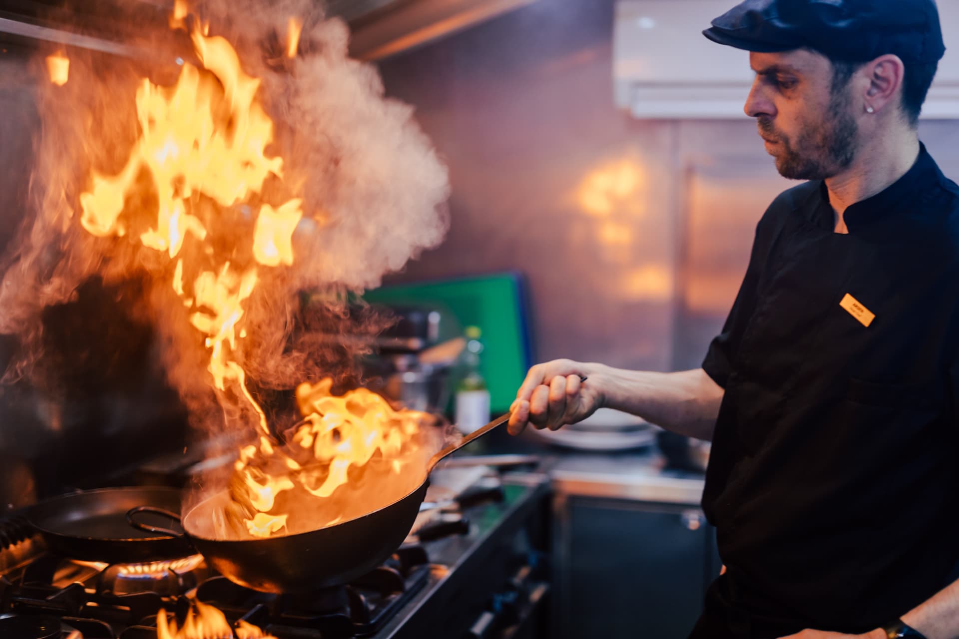 Chef flambéing food in a wok on a gas stove in a commercial kitchen setting