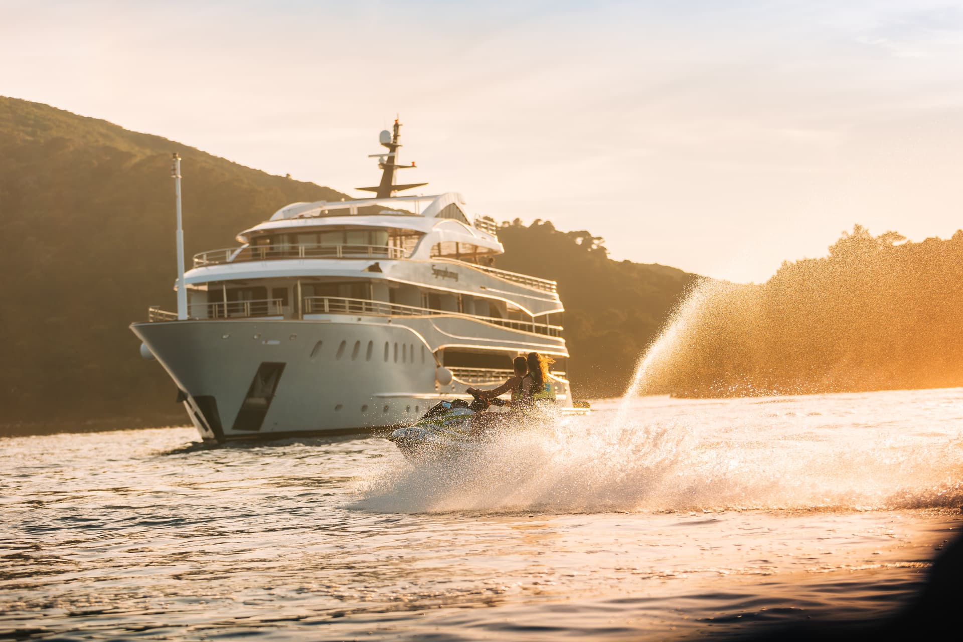 Jet skiing with large yacht and green hills in background at sunset