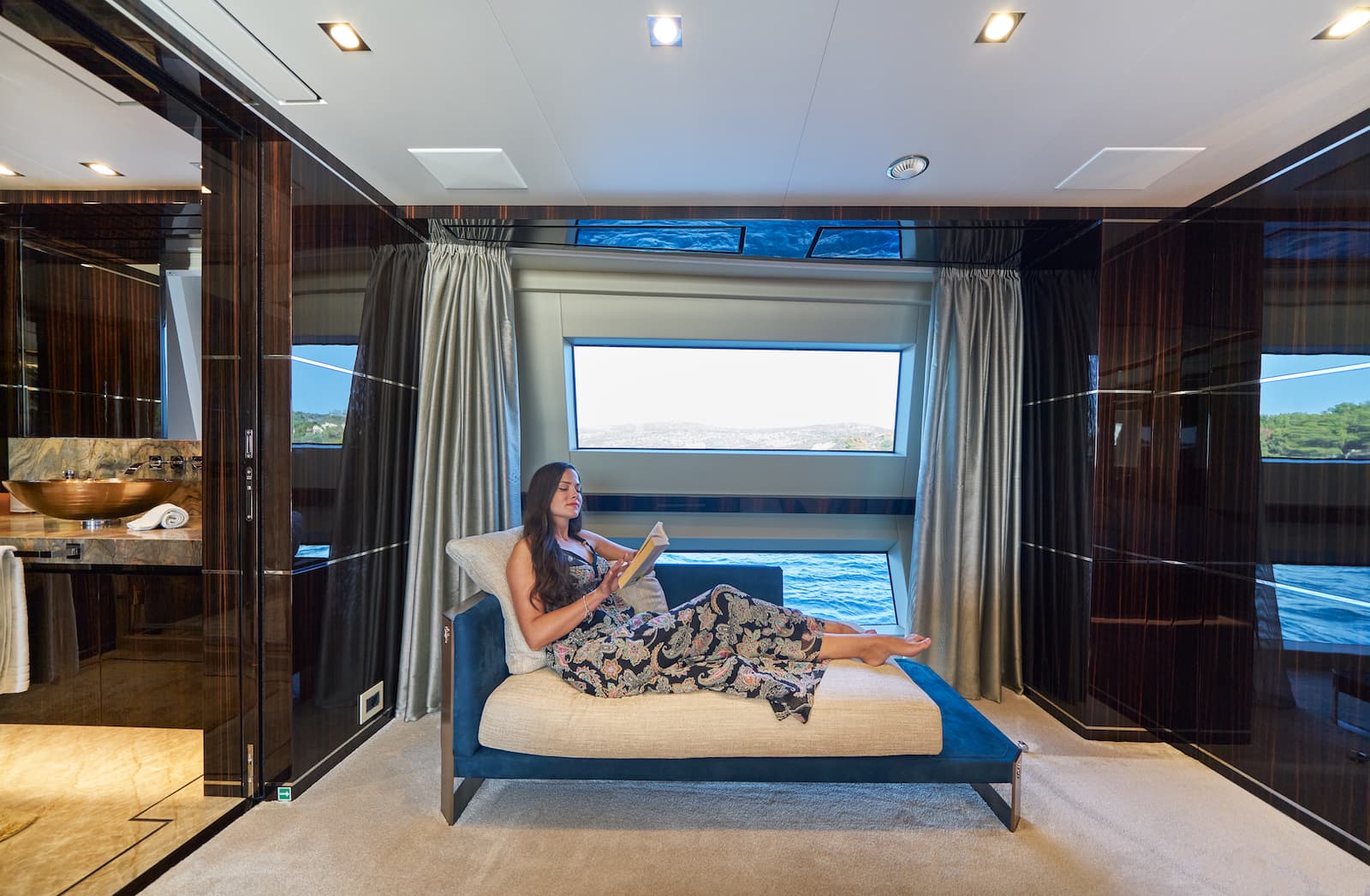 Woman reading on chaise lounge inside luxury yacht cabin with sea view