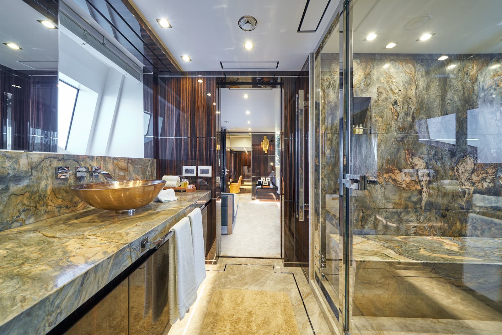 Luxury yacht bathroom with marble vanity, bronze vessel sink, and glass shower enclosure.
