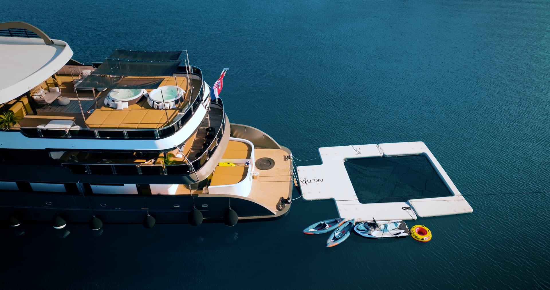 Luxury yacht docked with inflatable water toys and swim platform on deep blue water.