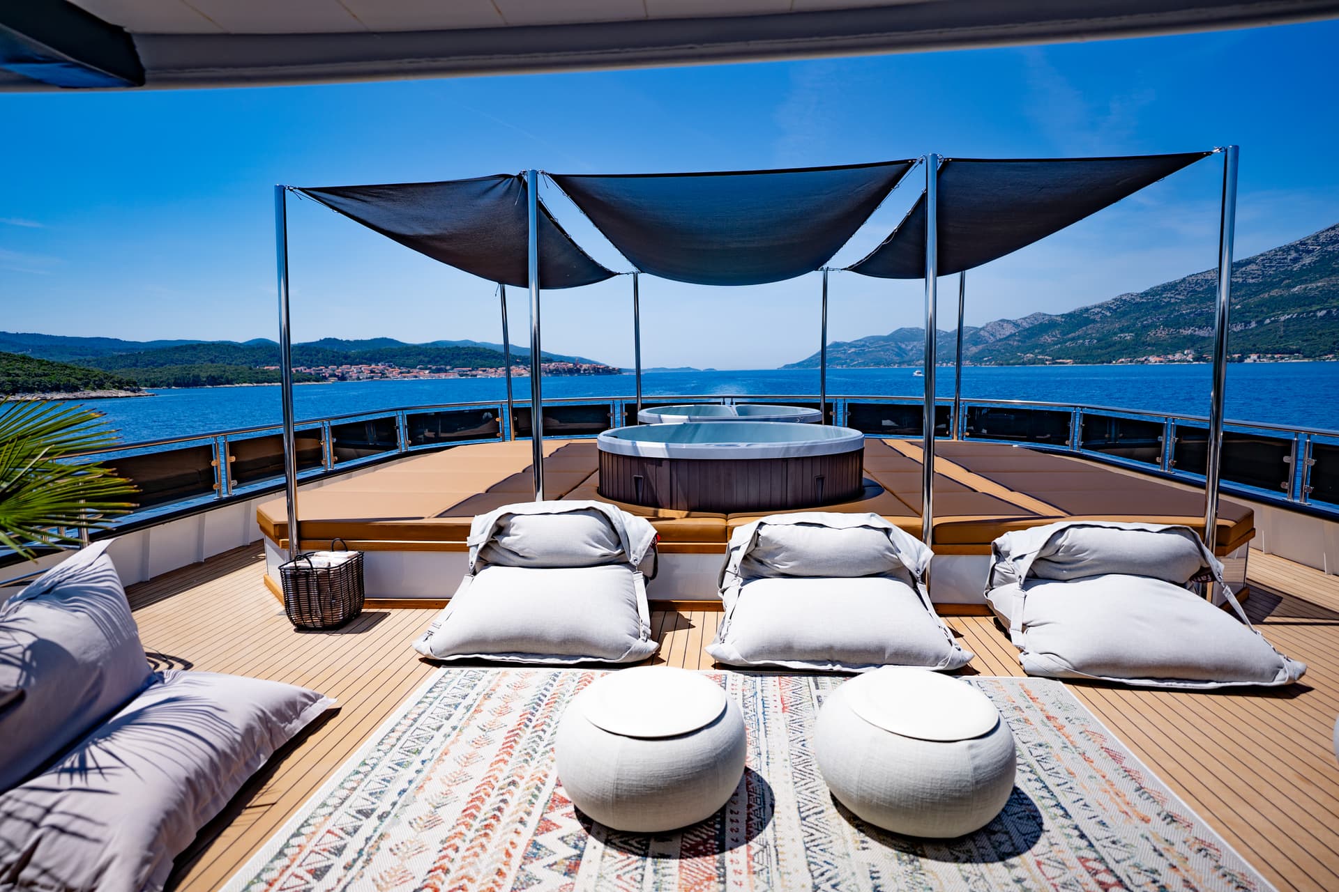 Yacht deck with hot tub, lounge chairs, and view of blue sea and green coastline.