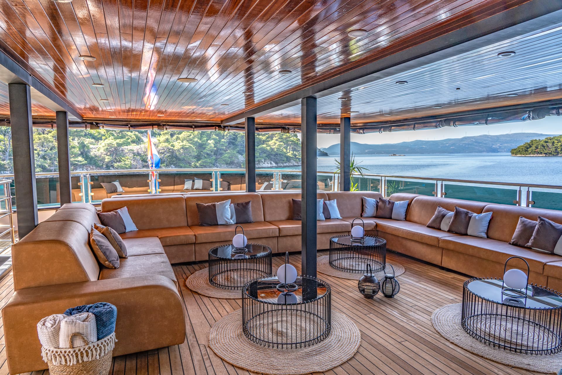 Lounge area on a boat deck with leather seating overlooking forested islands and blue sea.