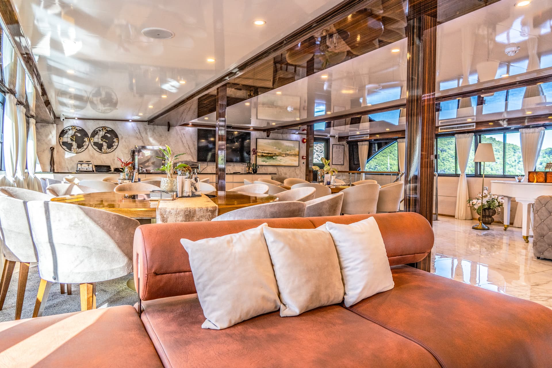 Lounge area with plush seating, dining tables, and windows showing lush green hills outside.