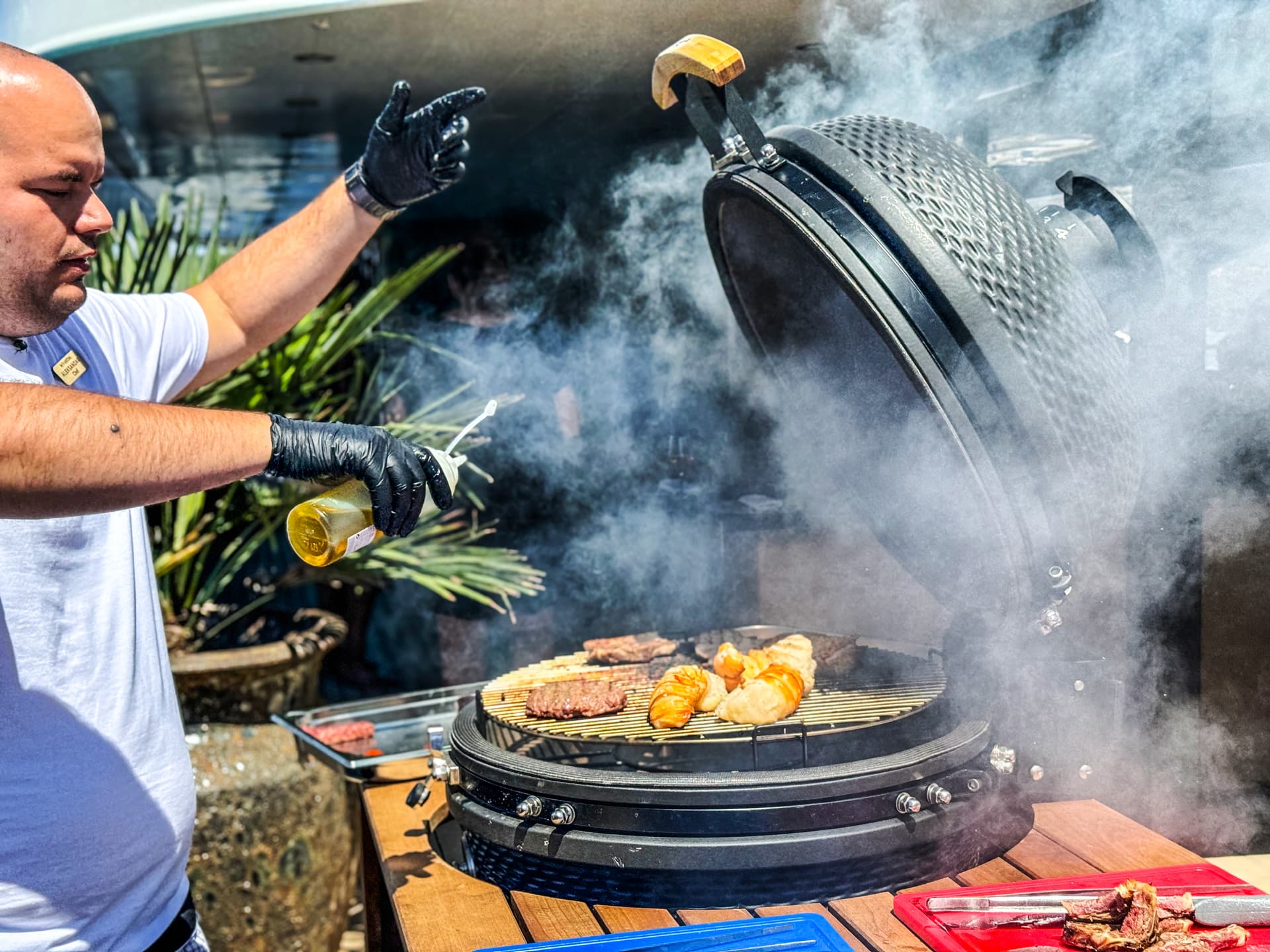 Man grilling burgers and bread on a smoker with smoke billowing outdoors.
