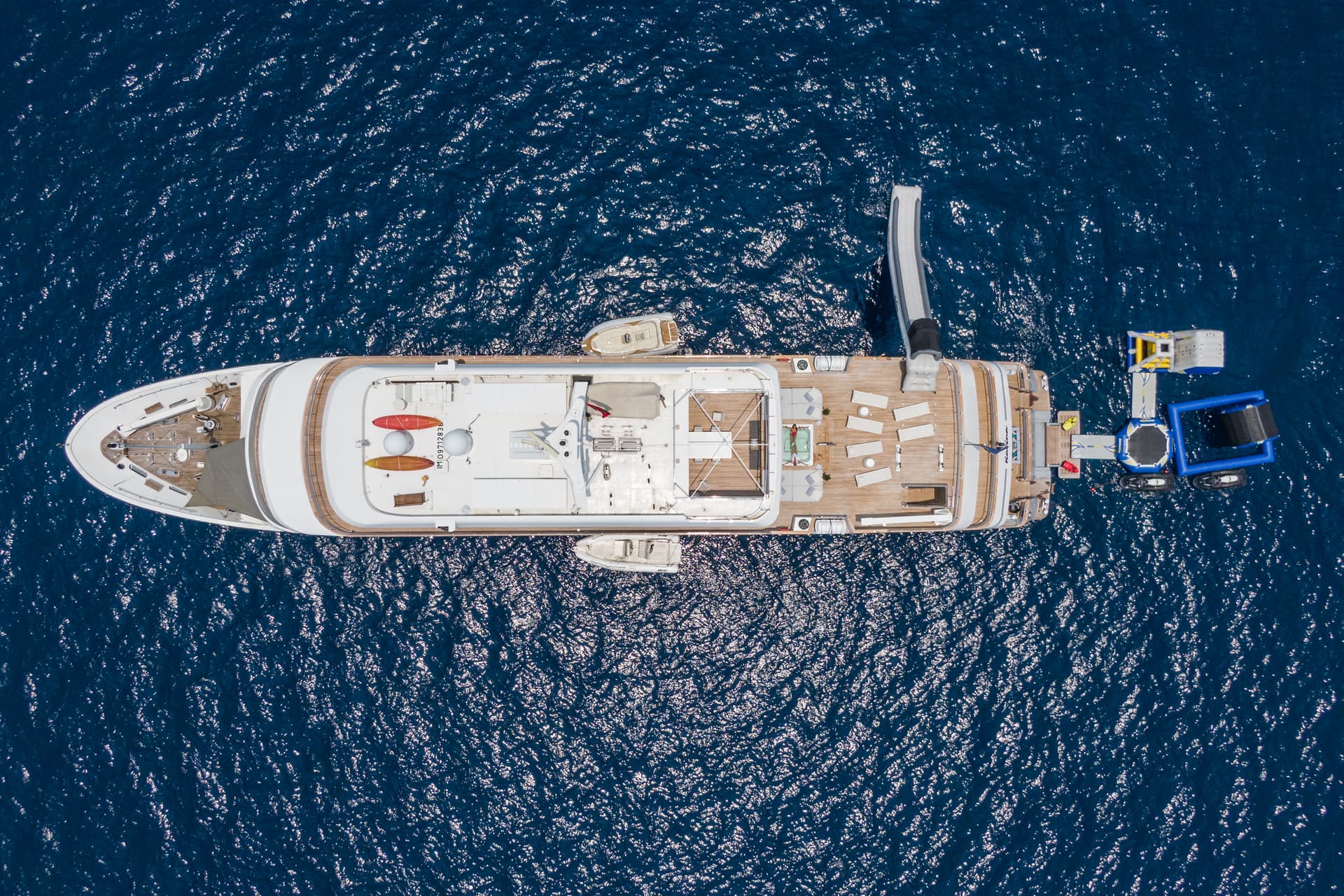 Aerial view of large white yacht anchored on deep blue sparkling water with inflatable water toys.