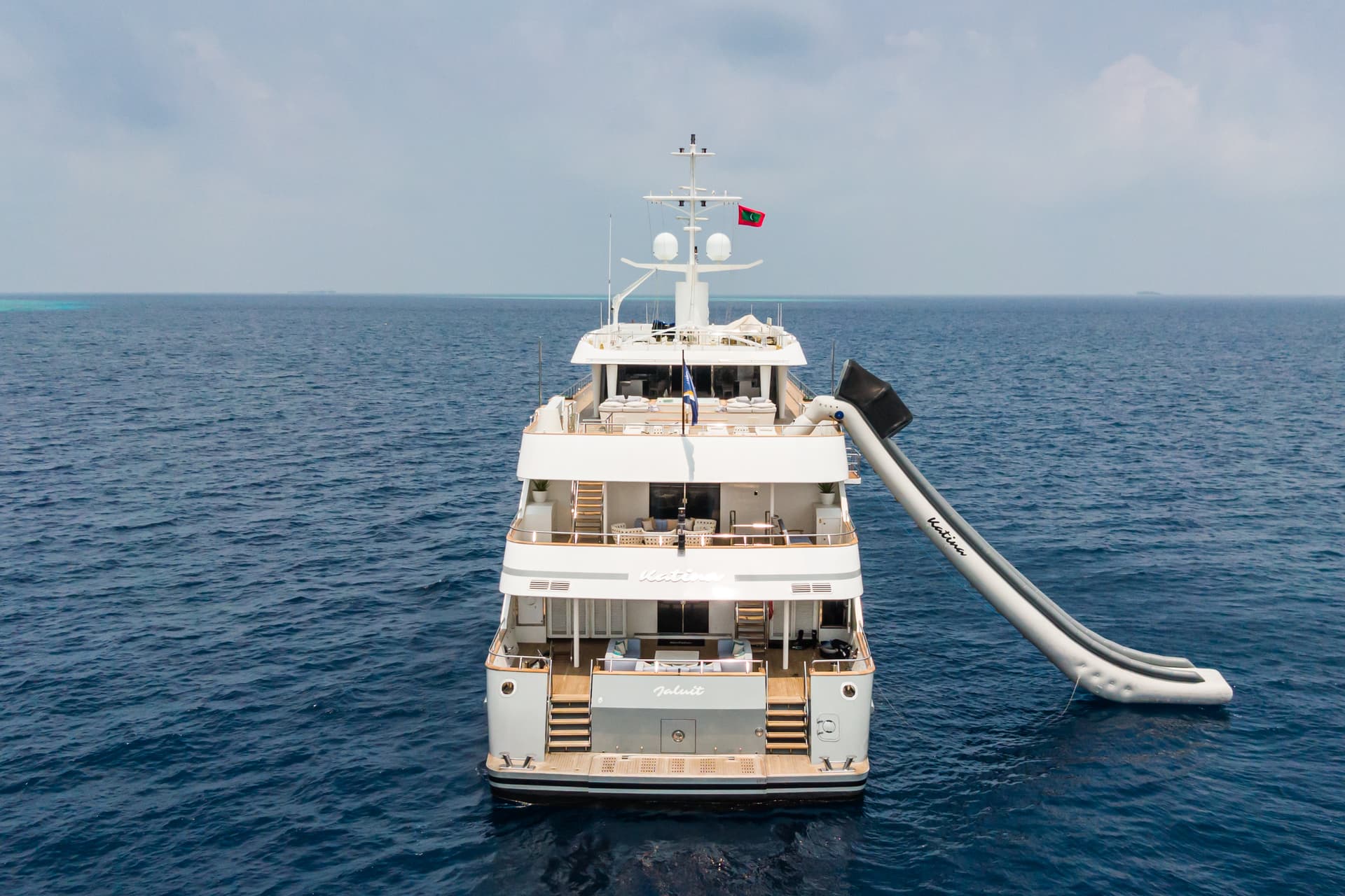Luxury yacht with inflatable slide floating on deep blue ocean water under cloudy sky.