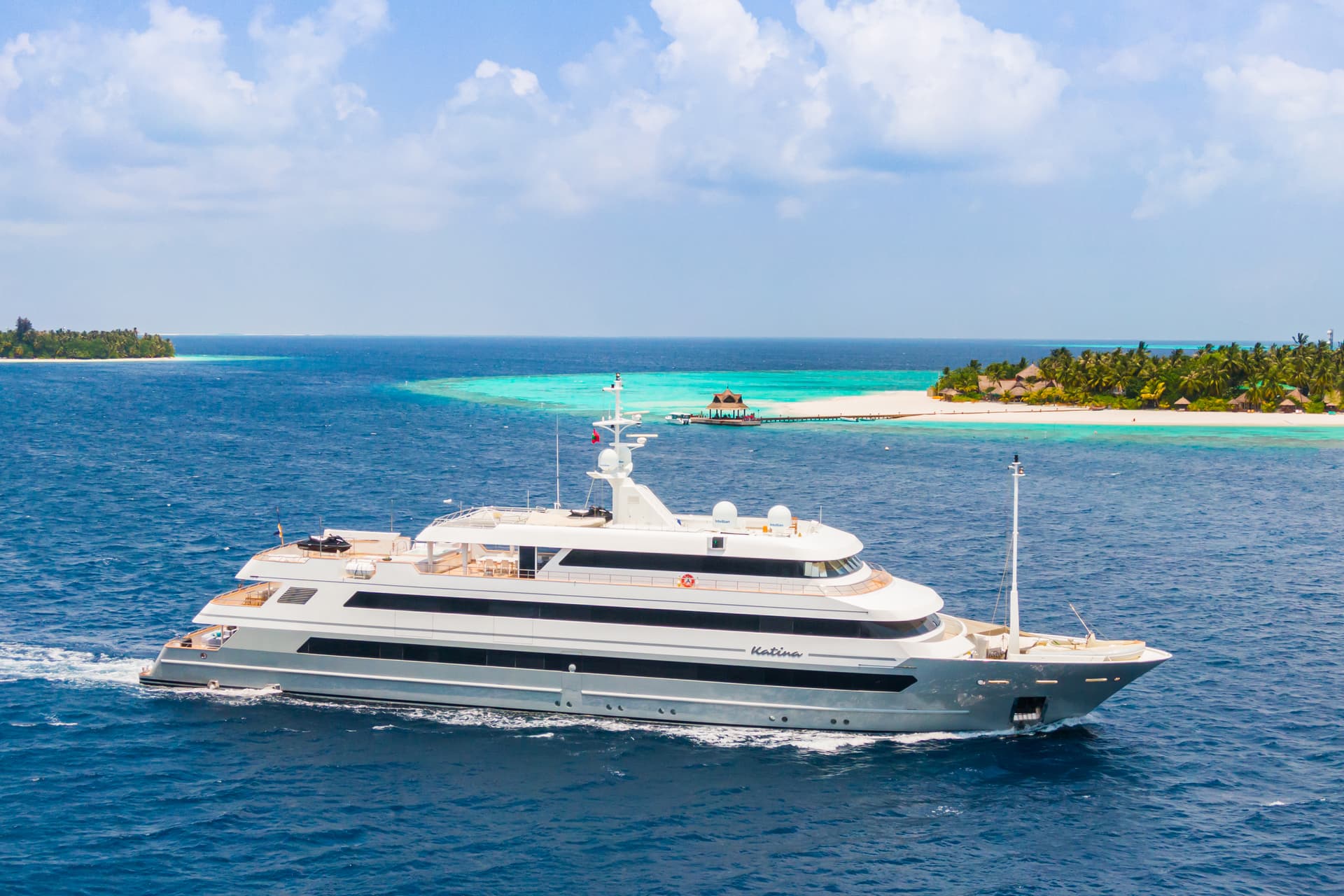 Luxury yacht sailing on deep blue water near a tropical island with white sand beach.