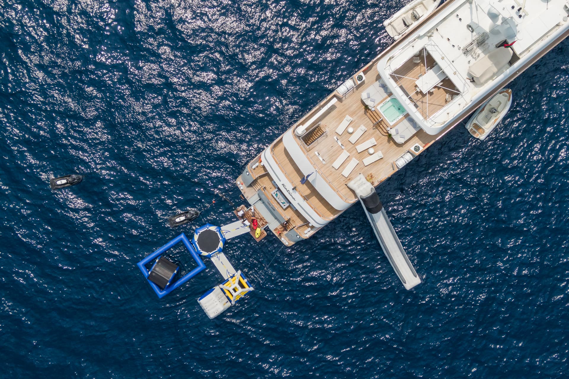 Luxury yacht anchored in deep blue water with inflatable water toys and a slide.