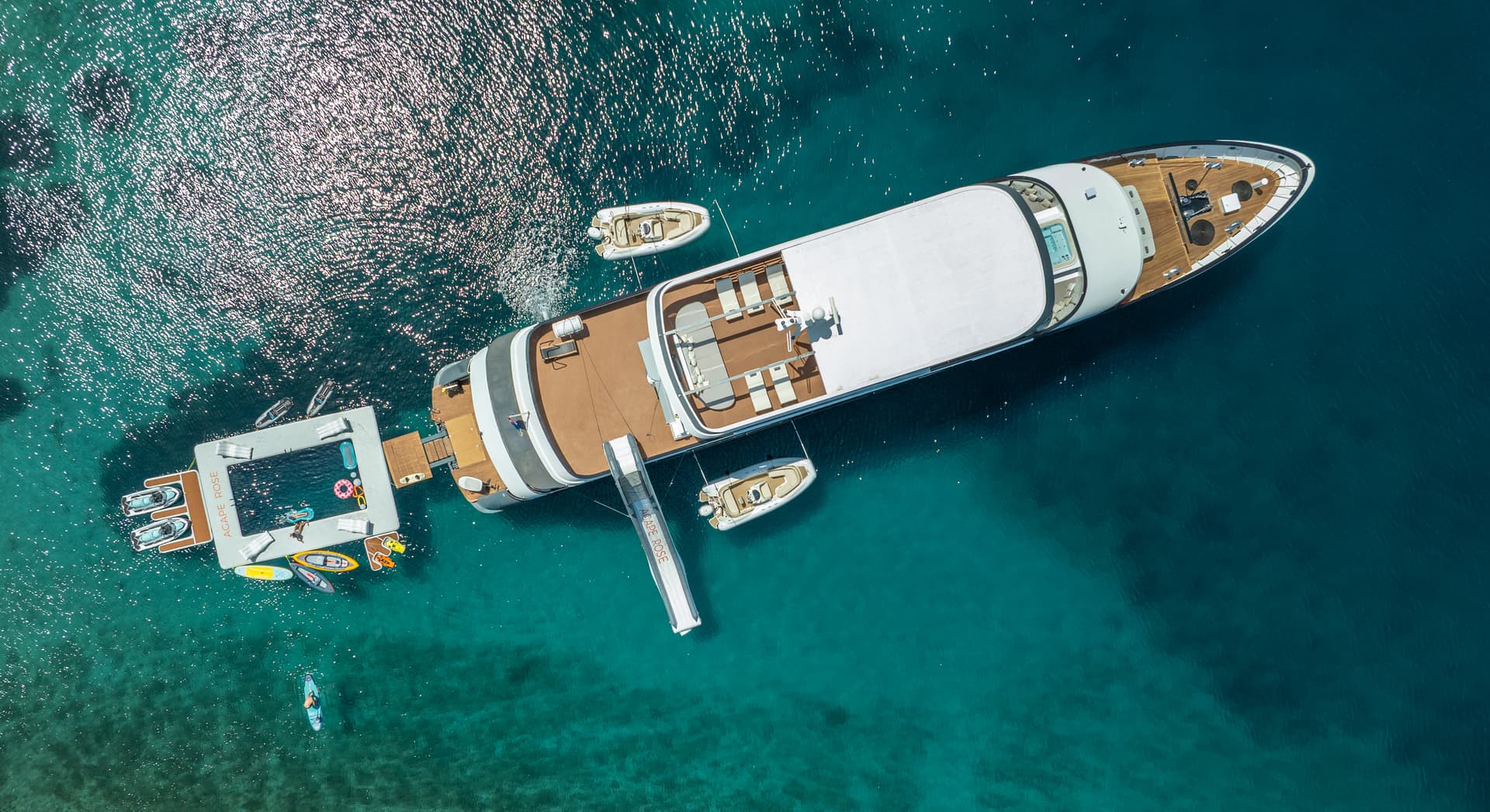 Aerial view of large yacht anchored near floating water platform with toys in clear turquoise sea.