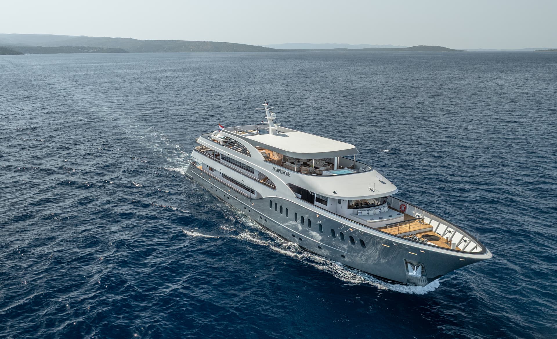 Large motor yacht cruising on deep blue sea near hilly coastline under bright sky