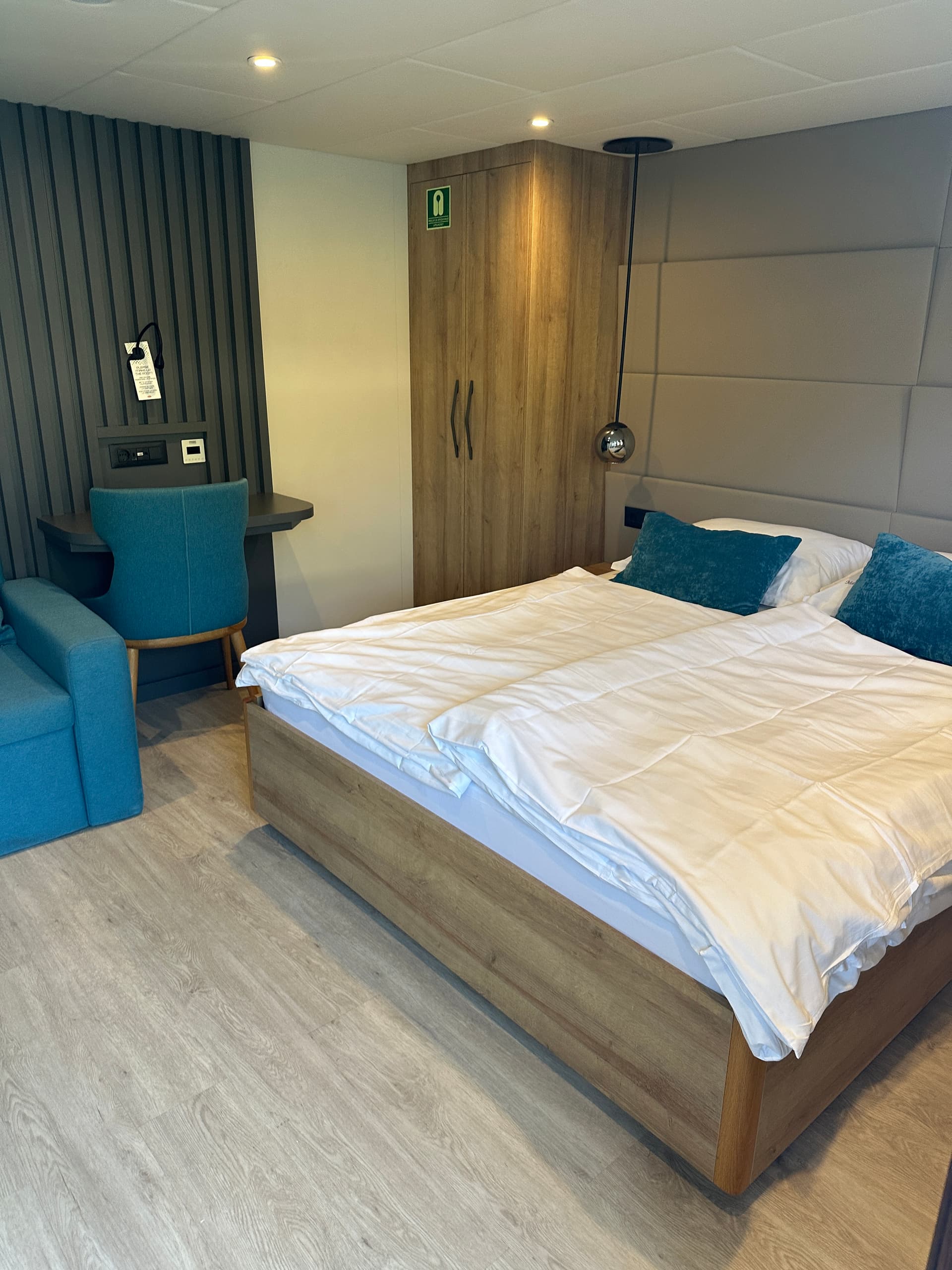 Modern ship cabin bedroom with double bed, teal accents, and wooden wardrobe.