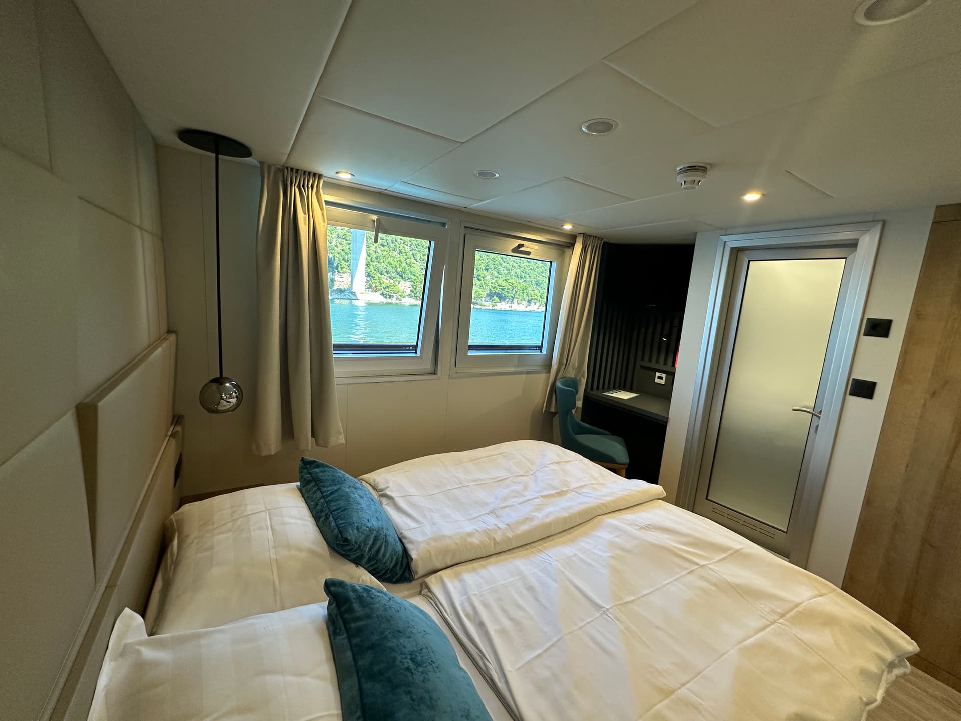 Cruise ship cabin with double bed and window view of water and greenery