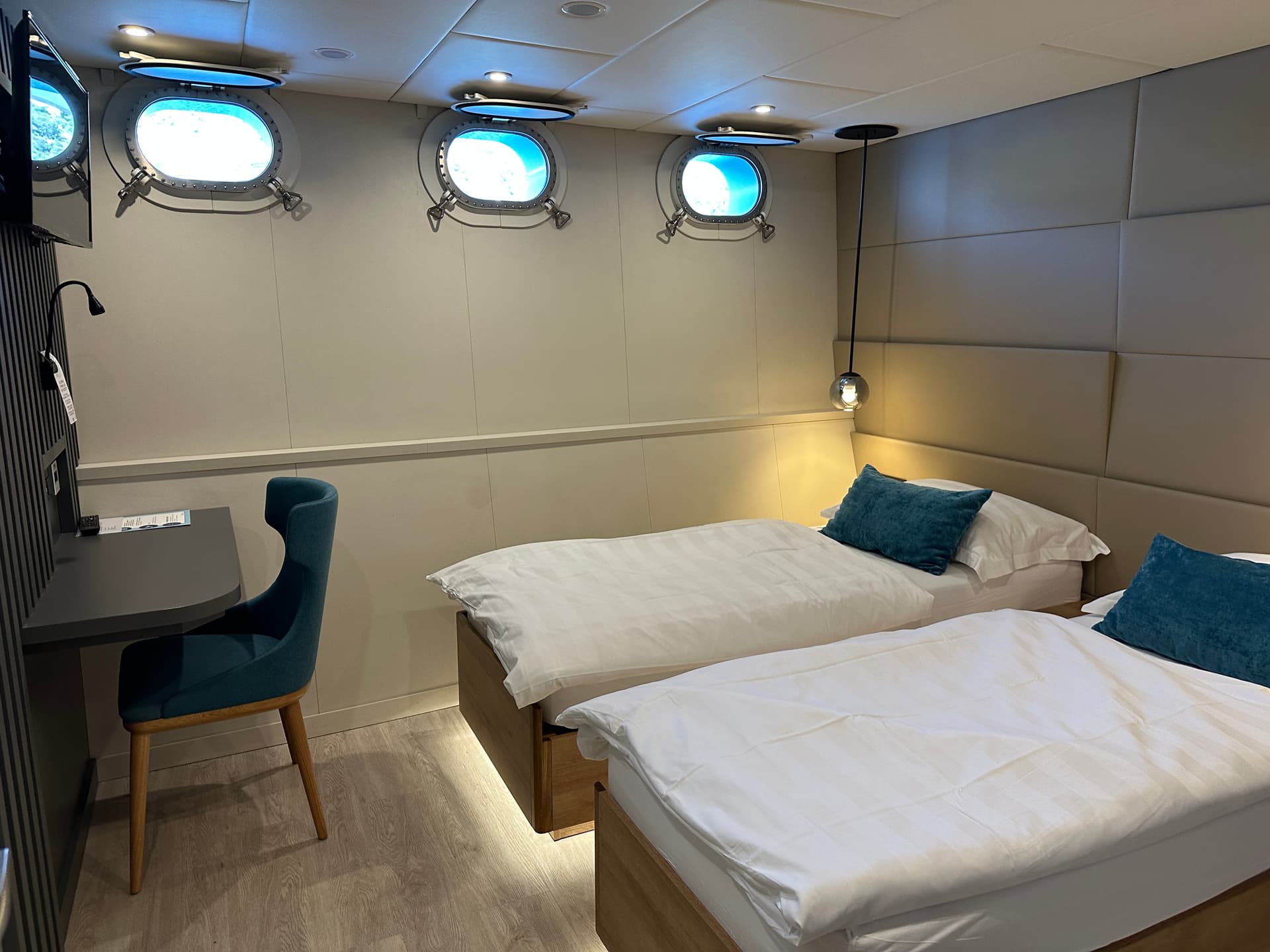 Ship cabin with twin beds, desk, chair, and portholes