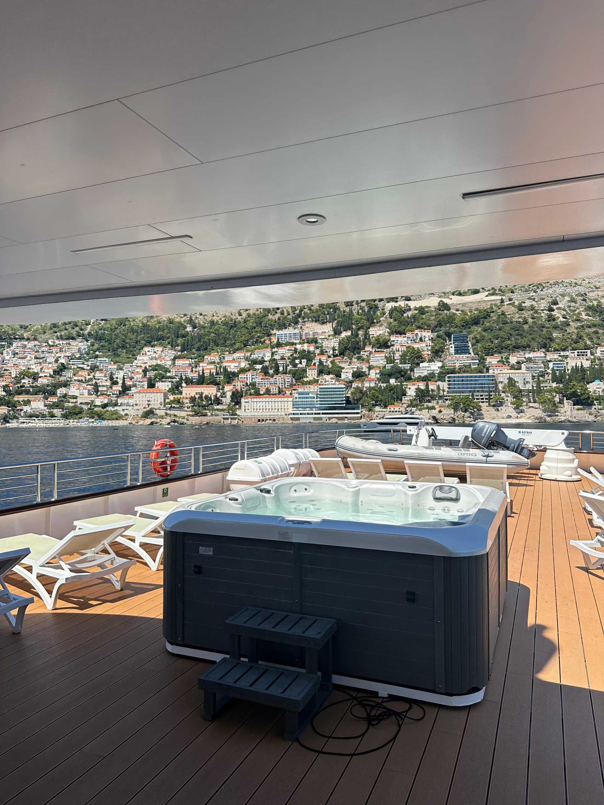 Wooden sundeck of a yacht with hot tub and lounge chairs overlooking a coastal town