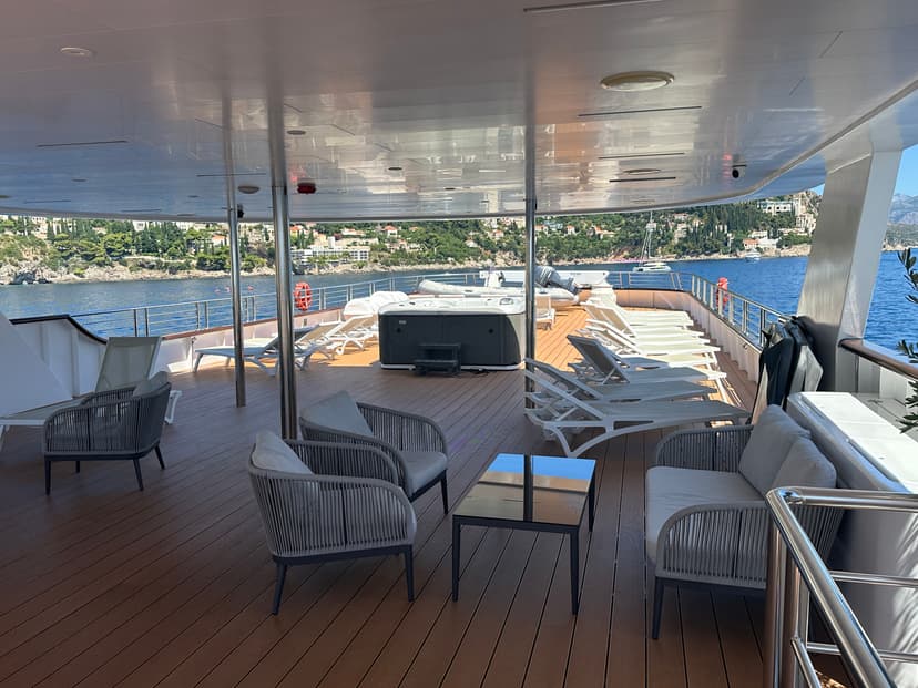 Wooden sundeck of a yacht with lounge chairs, hot tub, and ocean view